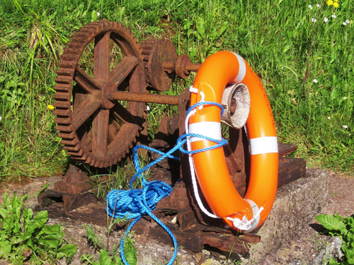 Rusting set of cogs in a mechanism. A life preserver ring is leaning against them.